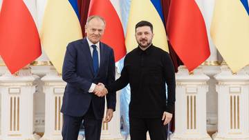 Premier Polski Donald Tusk i Prezydent Ukrainy Wołodymyr Zełenski ściskają sobie dłonie na tle flag Polski i Ukrainy.