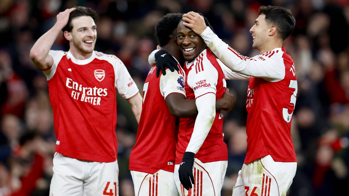 Piłkarze Arsenalu świętujący zwycięstwo, jeden z nich z ręką na głowie kolegi, wszyscy uśmiechnięci.