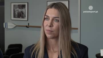 Anna Puławska, polska kajakarka, z blond włosami i niebieskimi oczami, w garniturze, podczas wywiadu. W tle widać obrazy i wiosło.