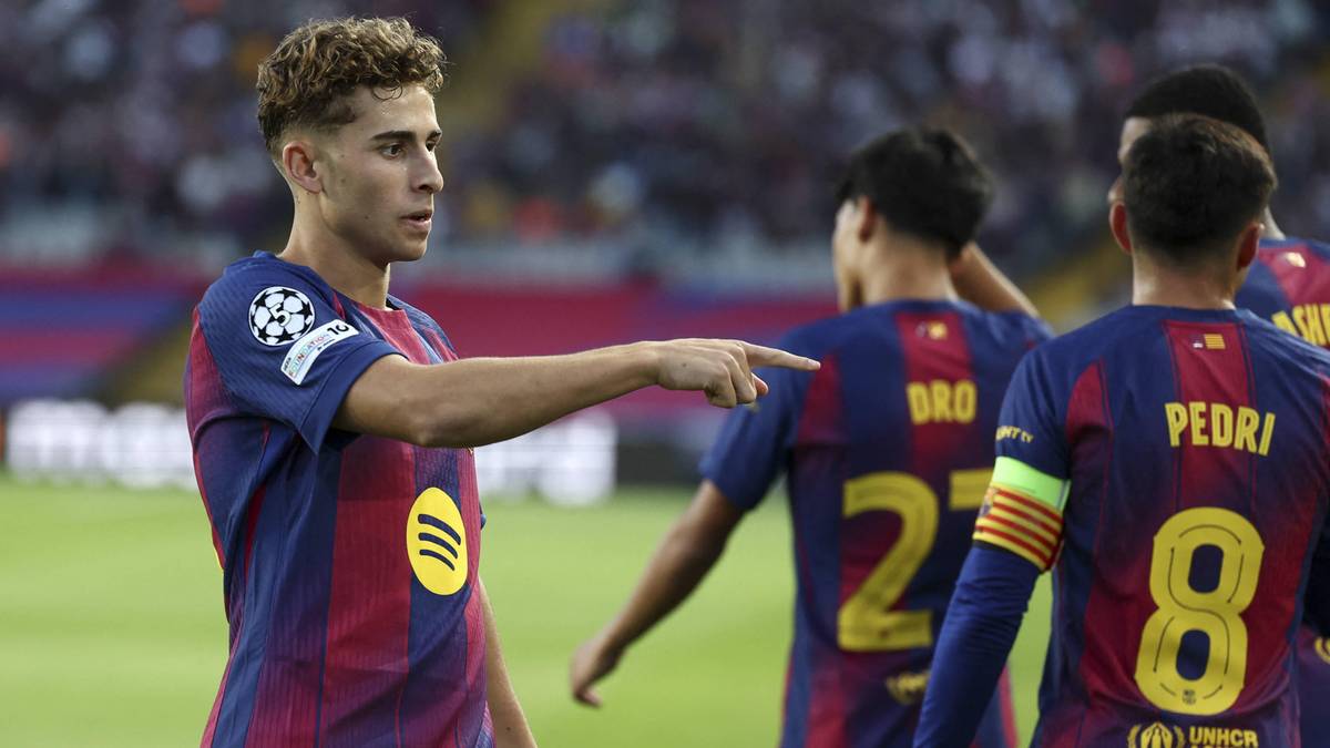 Piłkarz w niebiesko-bordowym stroju FC Barcelony, z numerem 2 na rękawie, wskazuje palcem w lewo, wydając polecenia innym zawodnikom na boisku.