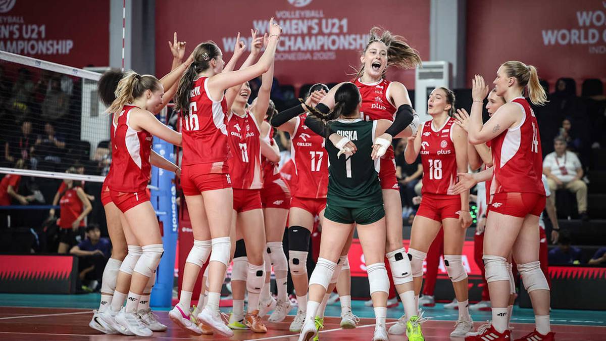 Siatkarki w czerwonych strojach celebrują zwycięstwo, jedna z nich z zielonym pasem na bluzce unosi ręce w geście radości.