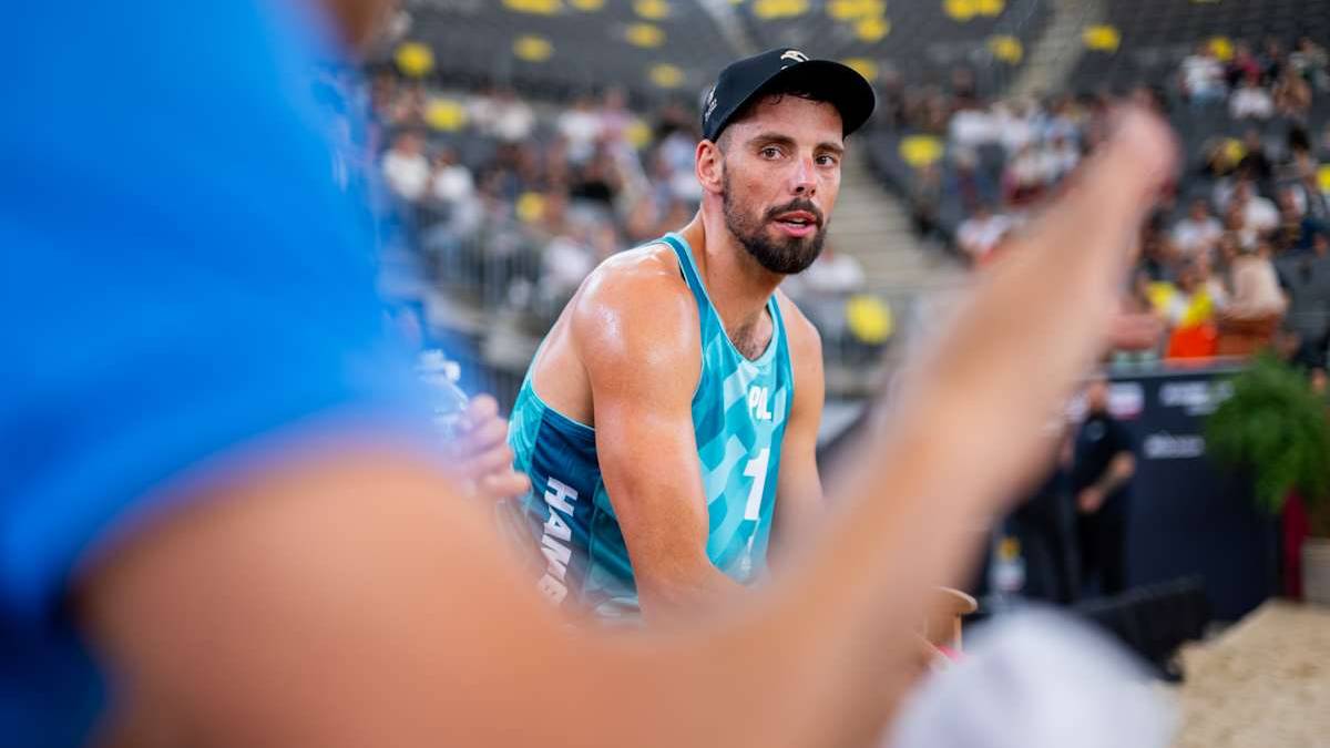 Młody siatkarz plażowy w czapce z daszkiem, w stroju sportowym, spogląda z uwagą na boisko.