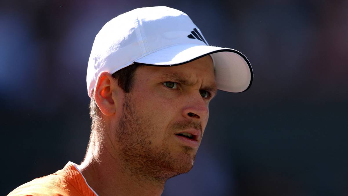 Portret tenisisty w białej czapce z daszkiem Adidas, ubranego w pomarańczową koszulkę.