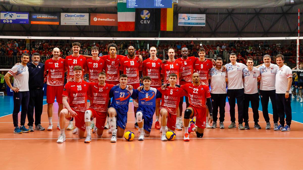 Drużyna siatkarska w czerwonych strojach pozuje do zdjęcia na boisku siatkarskim.