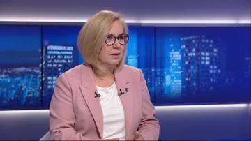 Kobieta w różowej marynarce i okularach siedzi w studiu telewizyjnym.