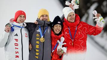 Czterech zawodnik&oacute;w w strojach sportowych z medalami na szyjach pozuje do zdjęcia na tle ośnieżonych stok&oacute;w.