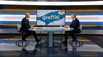 Dw&oacute;ch mężczyzn siedzi przy stole w studiu telewizyjnym. Na ekranie za nimi widnieje napis "graffiti".