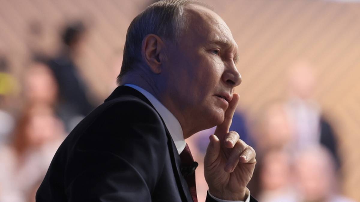 Portret Władimira Putina, prezydenta Rosji, w garniturze, z palcem wskazującym przy ustach.