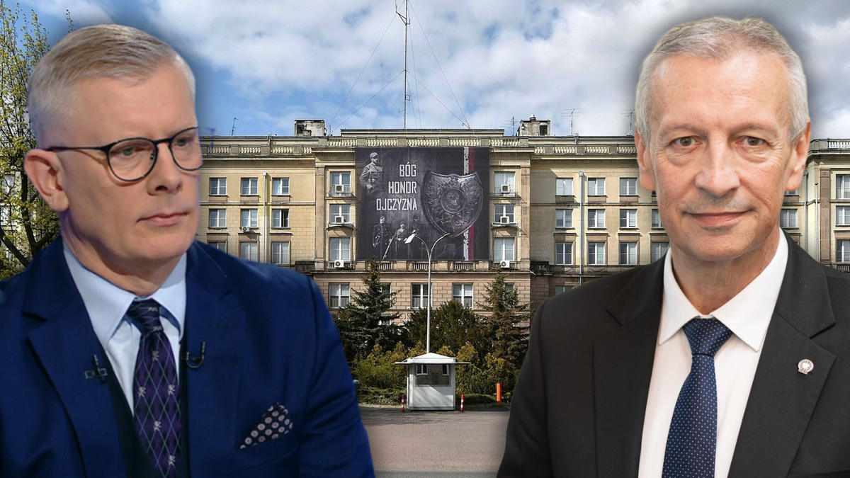 Dwaj mężczyźni w garniturach, jeden w okularach, na tle budynku z banerem.