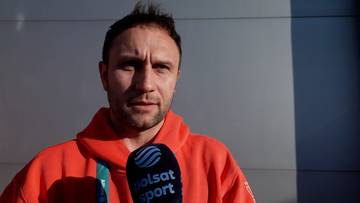 Mężczyzna w pomarańczowej bluzie z mikrofonem Polsat Sport.