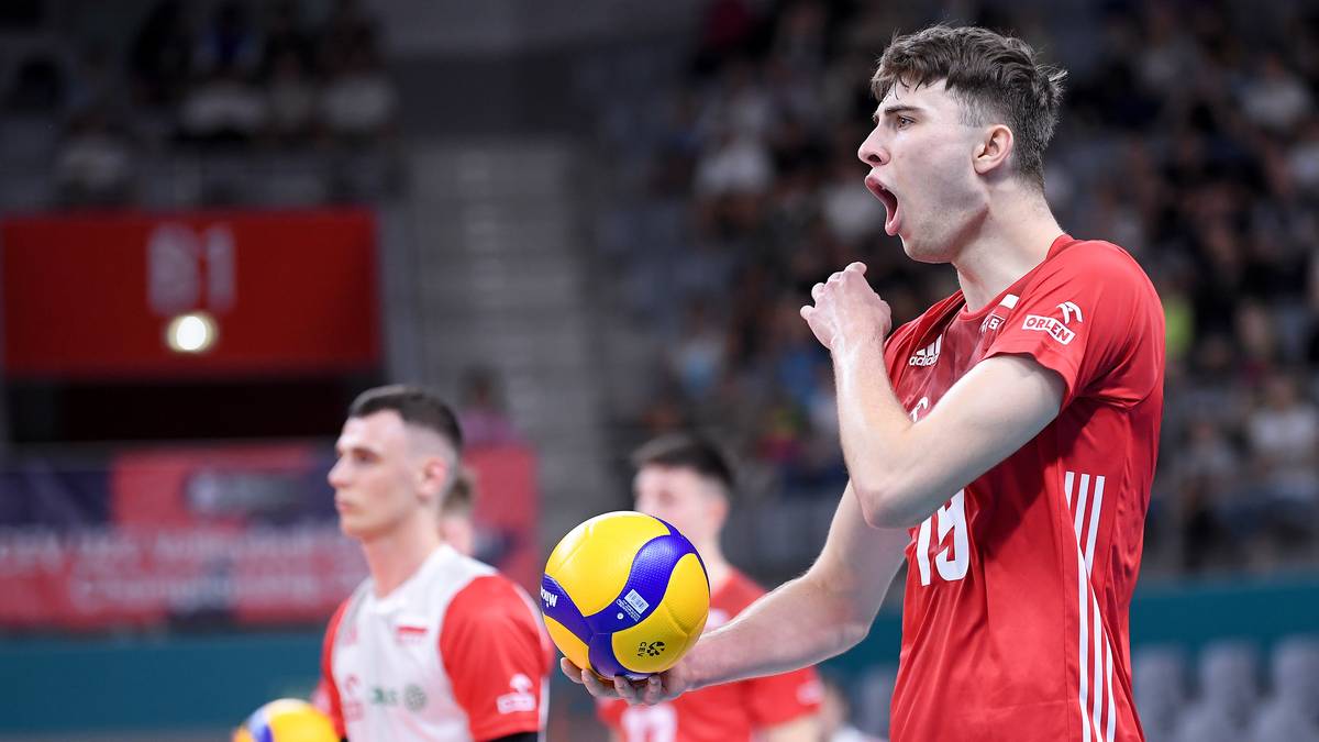 Siatkarz w czerwonej koszulce z numerem 13, krzyczy podczas meczu, trzymając piłkę.