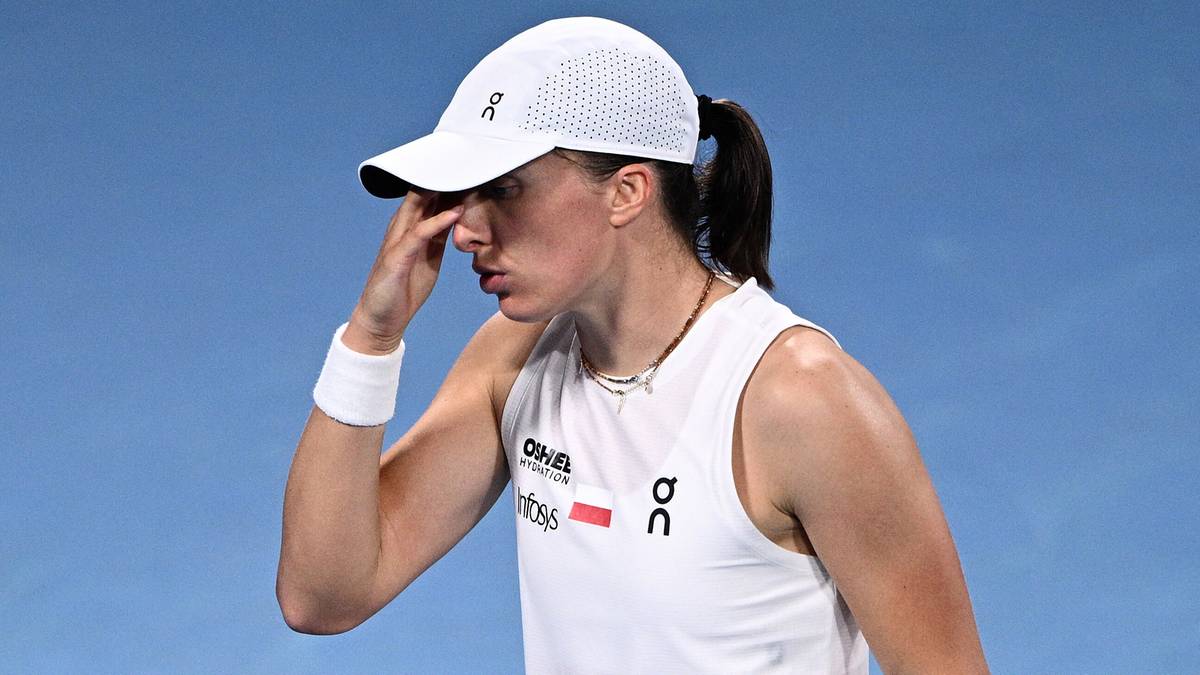 Iga Świątek w białej czapce i koszulce, dotykająca nosa.