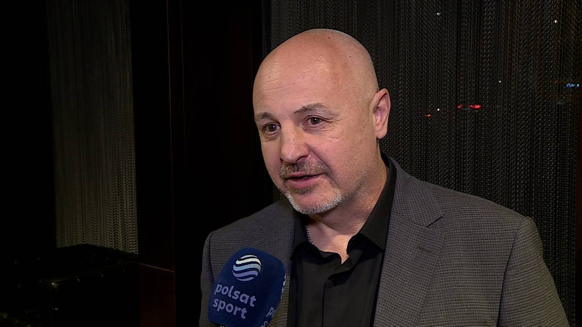 Mężczyzna z ogoloną głową i zarostem na twarzy w garniturze, m&oacute;wi do mikrofonu z logo Polsat Sport.