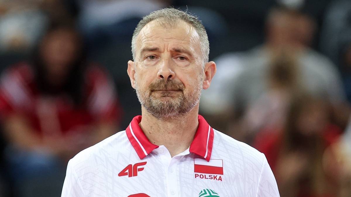 Portret mężczyzny z wąsami i kilkudniowym zarostem, ubranego w białą koszulkę polo z czerwonym kołnierzykiem. Na koszulce widnieje logo "4F" oraz flaga Polski z napisem "POLSKA". Tło jest rozmyte, sugerujące publiczność na wydarzeniu sportowym.