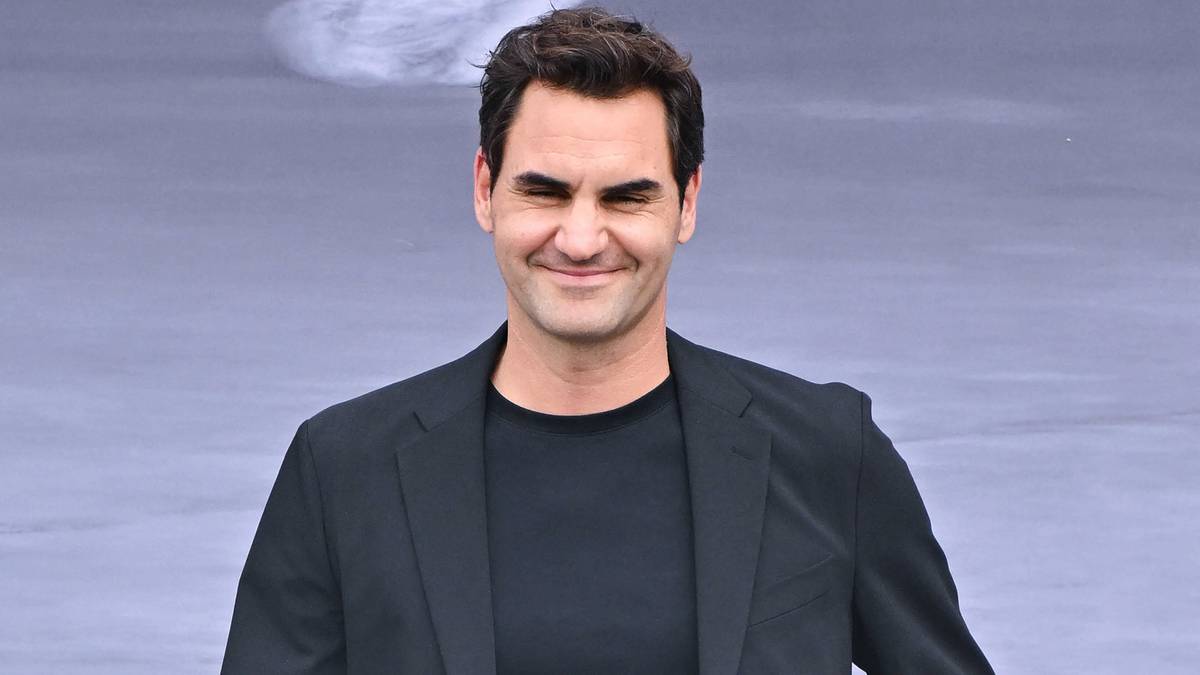 Roger Federer, uśmiechnięty mężczyzna w czarnej marynarce i czarnym t-shircie, na jasnym tle.
