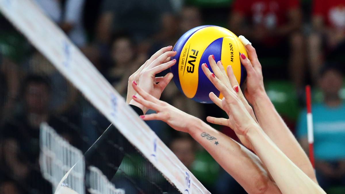 Dłonie siatkarek pr&oacute;bują przebić piłkę nad siatką podczas meczu.