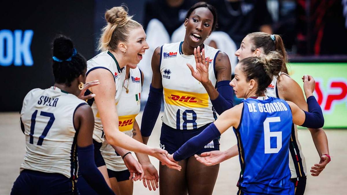 Pięć siatkarek w białych strojach sportowych, świętujących i dotykających się rękami, w tle publiczność.