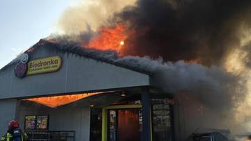 Płonący budynek sklepu Biedronka z gęstym dymem unoszącym się z dachu.