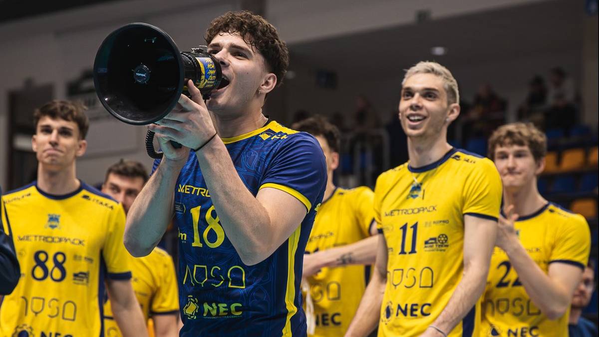 Siatkarz w stroju z numerem 18 przemawia przez megafon do zespołu w ż&oacute;łtych strojach sportowych.