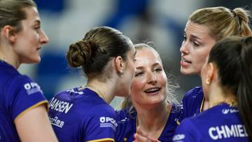 Grupa siatkarek w niebieskich strojach sportowych rozmawia ze sobą na boisku.