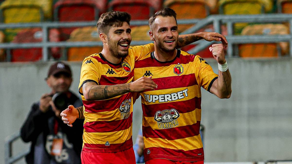 Dwóch piłkarzy w żółto-czerwonych strojach cieszy się z gola, obejmując się ramionami.