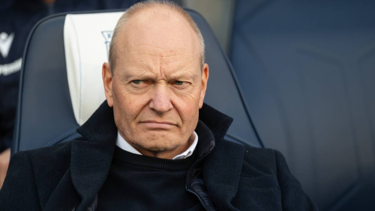 Starszy mężczyzna o surowym wyrazie twarzy siedzi na krześle.