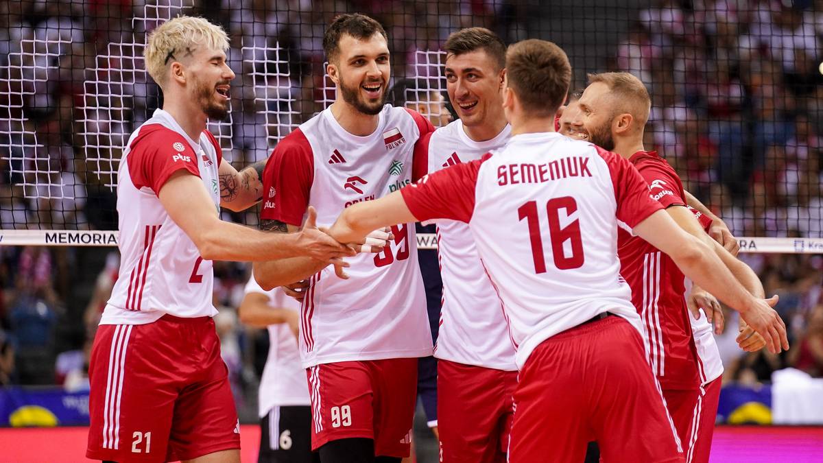 Siatkarze w białych koszulkach z czerwonymi elementami i białych spodenkach cieszą się po meczu, podając sobie ręce.