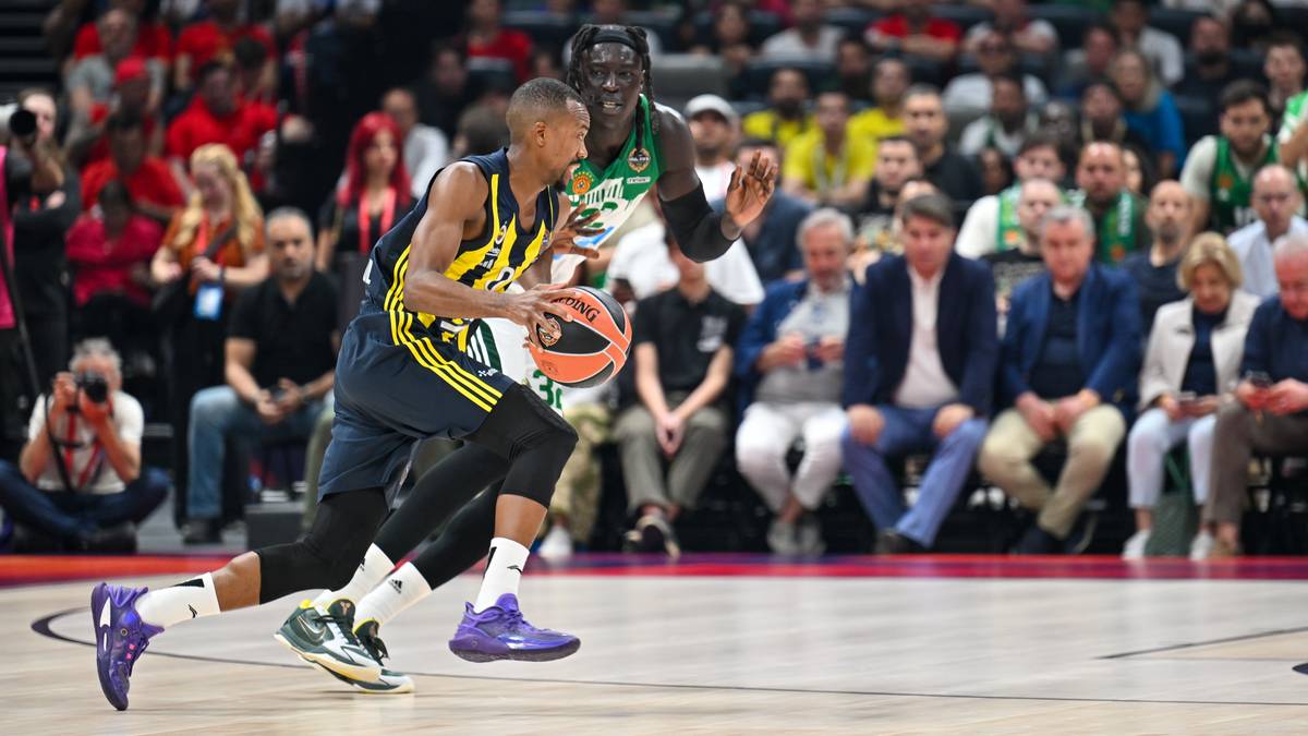 Koszykarz AS Monaco z piłką w rękach, w pozie do podania lub rzutu, w trakcie meczu przeciwko Fenerbahce. W tle widownia na trybunach.