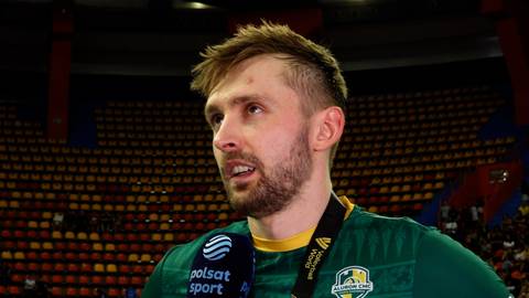 Portret Mateusza Bienka, polskiego siatkarza, w zielonej koszulce z widoczną opaską z logo Polsat Sport. Tło stanowi trybuna stadionu wypełniona widzami.