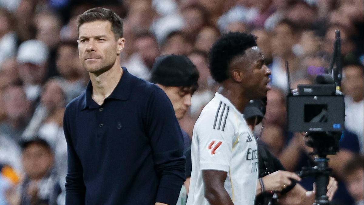 Trener Xabi Alonso i piłkarz Vinicius Jr. stojący obok siebie na boisku piłkarskim, na tle tłumu kibic&oacute;w.