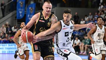 Dwóch zawodników drużyny koszykarskiej walczy o piłkę na boisku.