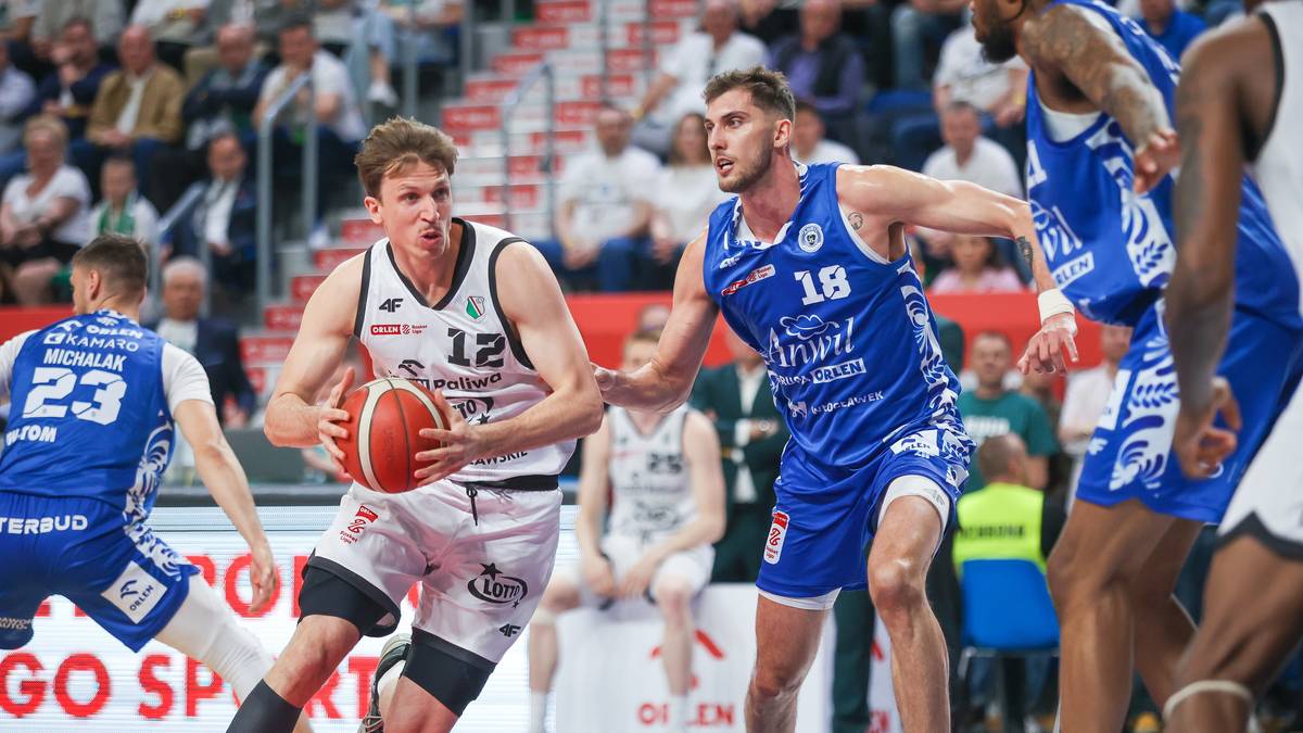 Dwóch zawodników drużyny Anwil w akcji podczas meczu koszykówki. Jeden z nich, w białej koszulce z numerem 12, prowadzi piłkę, podczas gdy drugi, w niebieskiej koszulce z numerem 18, próbuje go zatrzymać. W tle widownia i inni gracze.