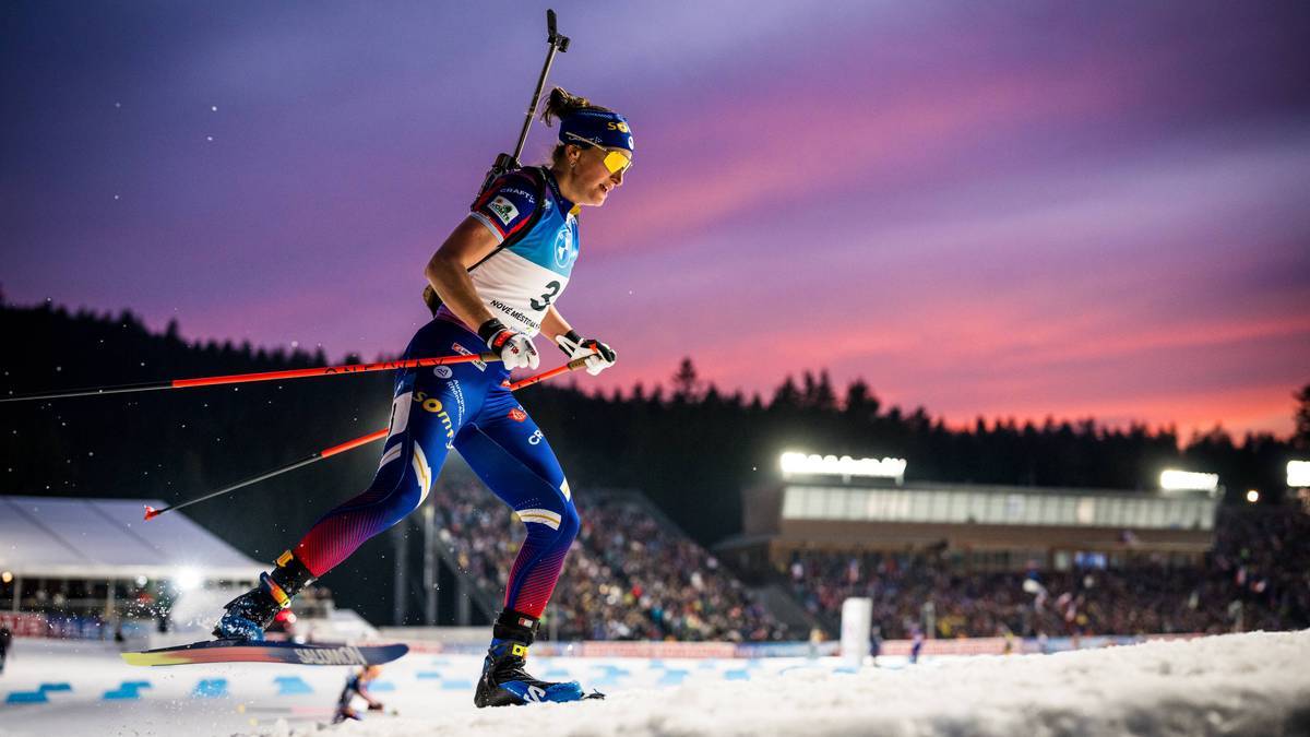 Biathlonistka w akcji na tle zachodzącego słońca.