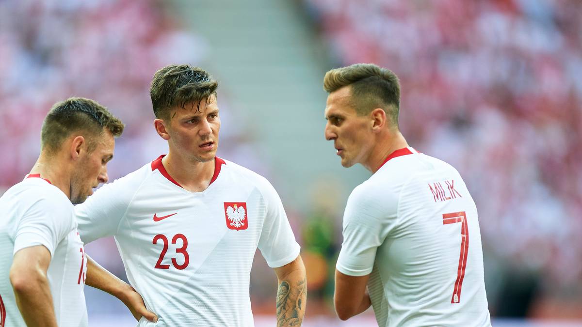 Trzech piłkarzy reprezentacji Polski w białych strojach z czerwonymi spodenkami.