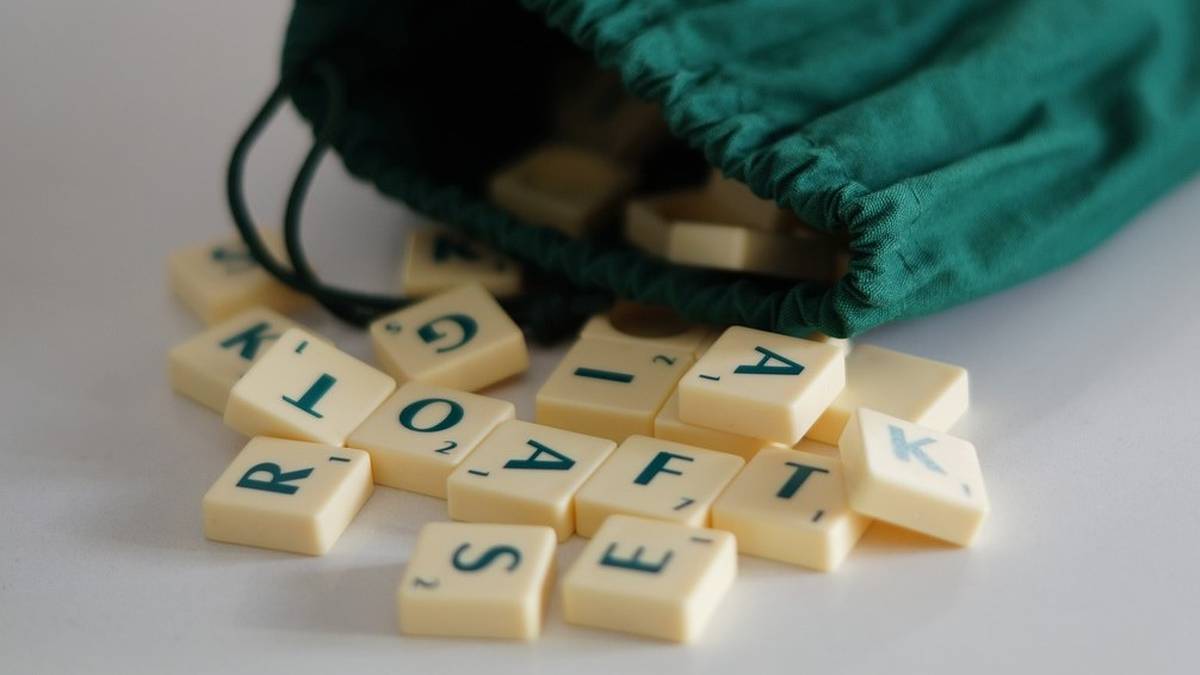 Rozsypane kostki z literami przypominające grę Scrabble, wyjęte z zielonego woreczka.