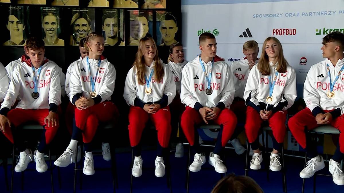 Grupa młodych sportowców w białych bluzach z białoczerwonymi elementami i czerwonych spodniach, siedzących na krzesłach i prezentujących swoje medale.