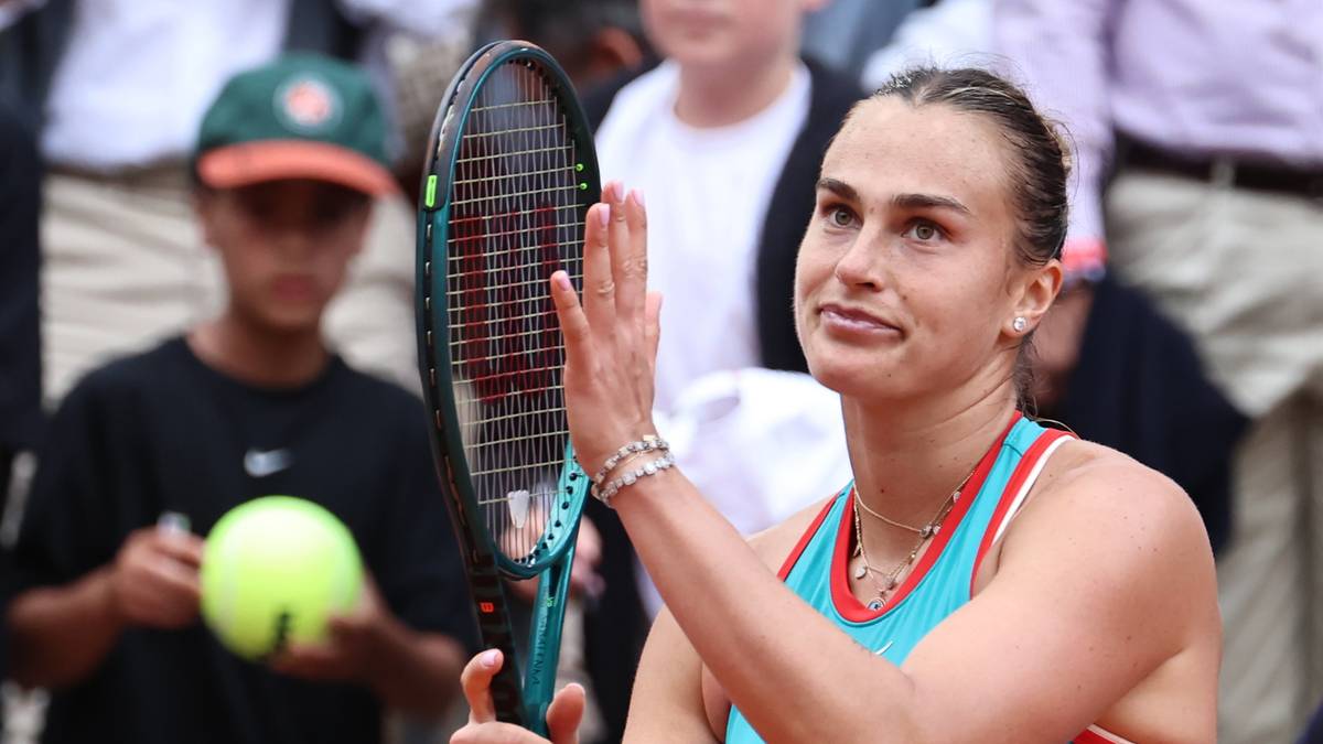 Aryna Sabalenka uśmiecha się trzymając rakietę tenisową w prawej dłoni, patrząc w bok.