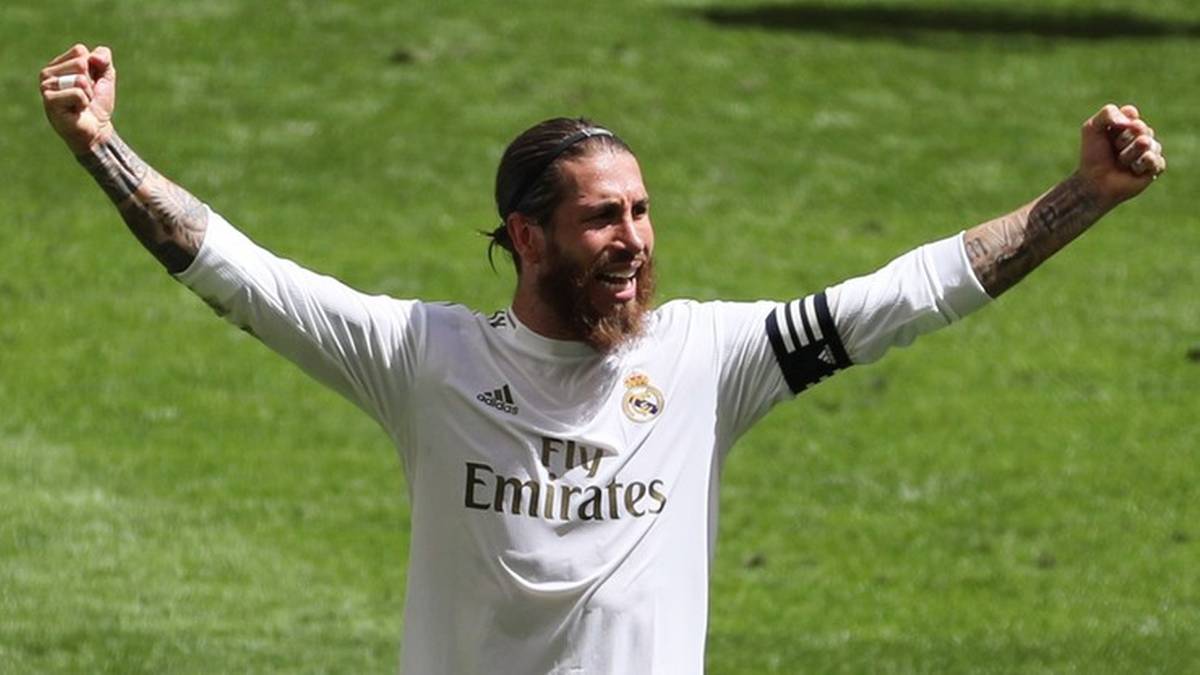 Piłkarz Sergio Ramos w białej koszulce Realu Madryt z uniesionymi rękami w geście triumfu na zielonej murawie stadionu.