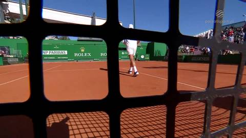 Tenisista na korcie ziemnym, w tle zielone bandy z logotypami sponsor&oacute;w.