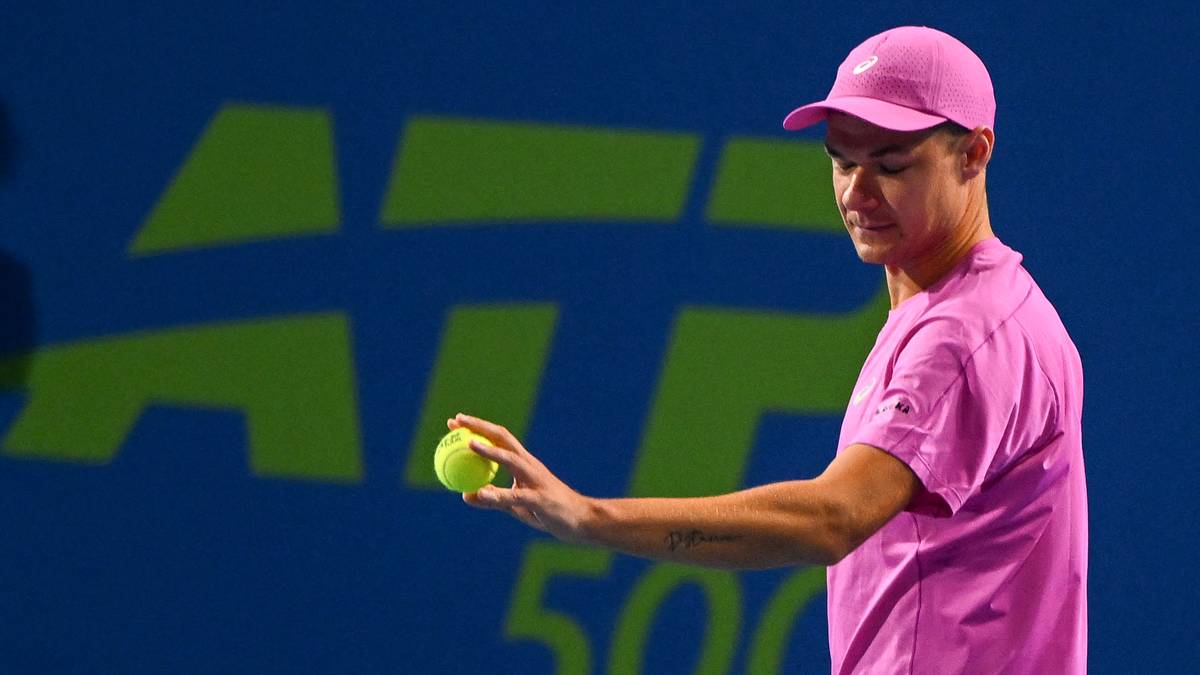 Tenisista Kamil Majchrzak w r&oacute;żowej koszulce i czapce, trzymający piłkę tenisową, z logo ATP w tle.