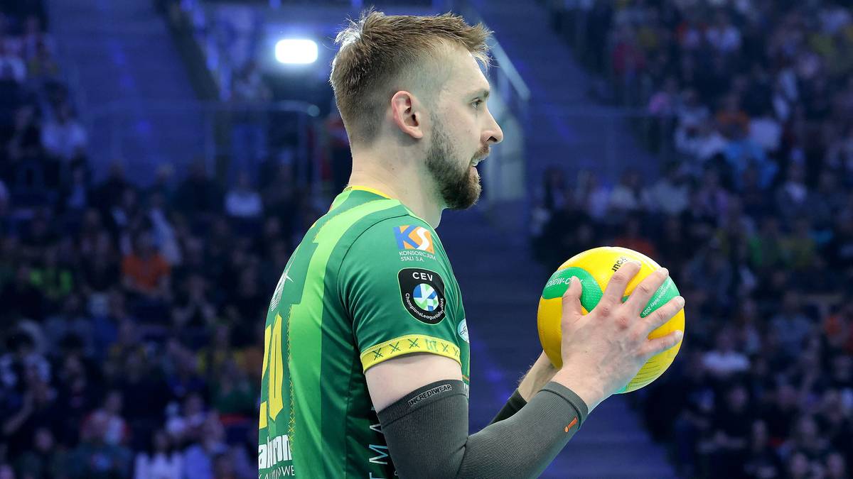 Mężczyzna w zielonej koszulce sportowej trzymający żółto-zieloną piłkę do siatkówki.