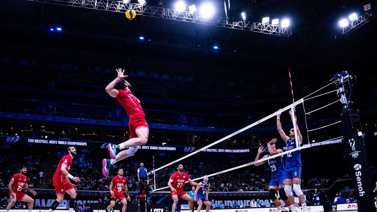 Siatkarz w skoku atakuje piłkę nad siatką, podczas meczu siatkówki.