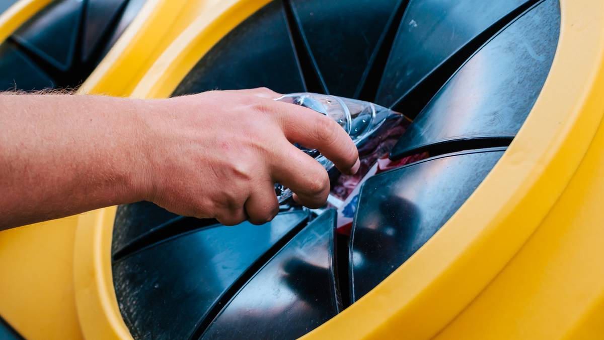 Dłoń wrzuca plastikową butelkę do ż&oacute;łtego pojemnika na odpady.