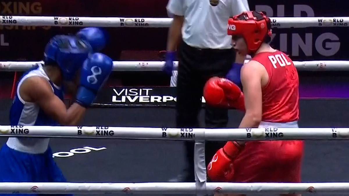 Dwie kobiety w rękawicach bokserskich walczą na ringu. Jedna zawodniczka ma na sobie niebieski strój i kask, druga czerwony strój i kask z napisem "POL".