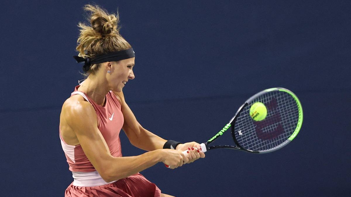 Kobieta w stroju tenisowym z rakietą w ręku, w trakcie uderzenia piłki.