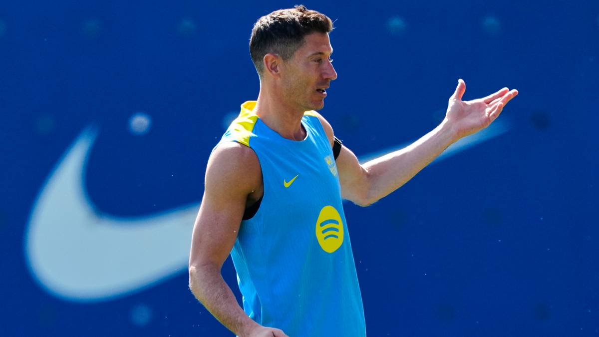 Piłkarz FC Barcelony Robert Lewandowski w niebieskiej koszulce treningowej, z gestem wskazującym ręką.