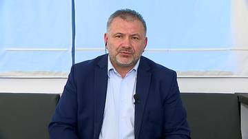 Mężczyzna w średnim wieku w granatowej marynarce i białej koszuli siedzi na kanapie, patrząc w obiektyw kamery.