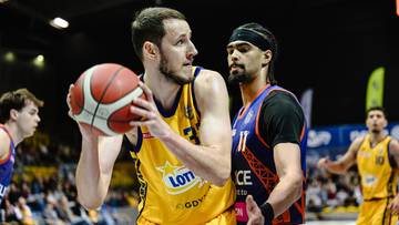 Koszykarz w ż&oacute;łtej koszulce z piłką w rękach, obok niego stoi zawodnik w niebieskiej koszulce