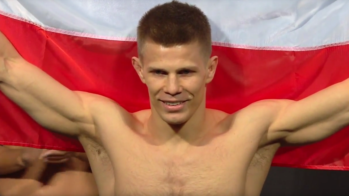 Mężczyzna z flagą Polski za plecami, uśmiechający się.