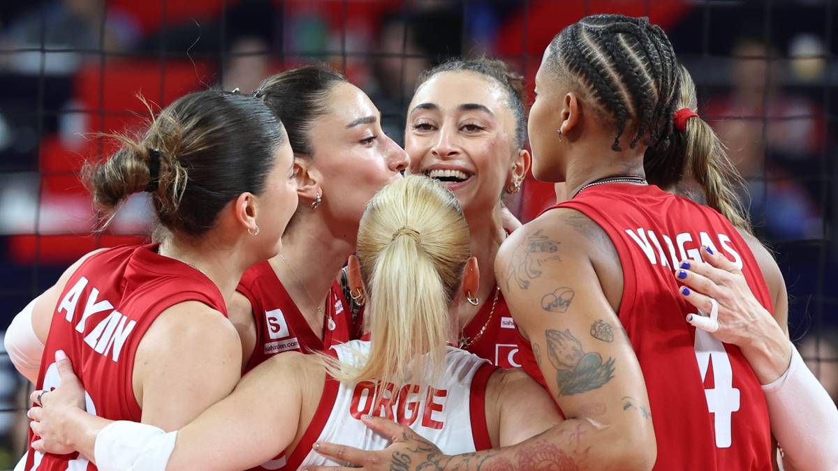 Grupa zawodniczek siatk&oacute;wki w czerwonych strojach świętuje zwycięstwo, przytulając się i śmiejąc.